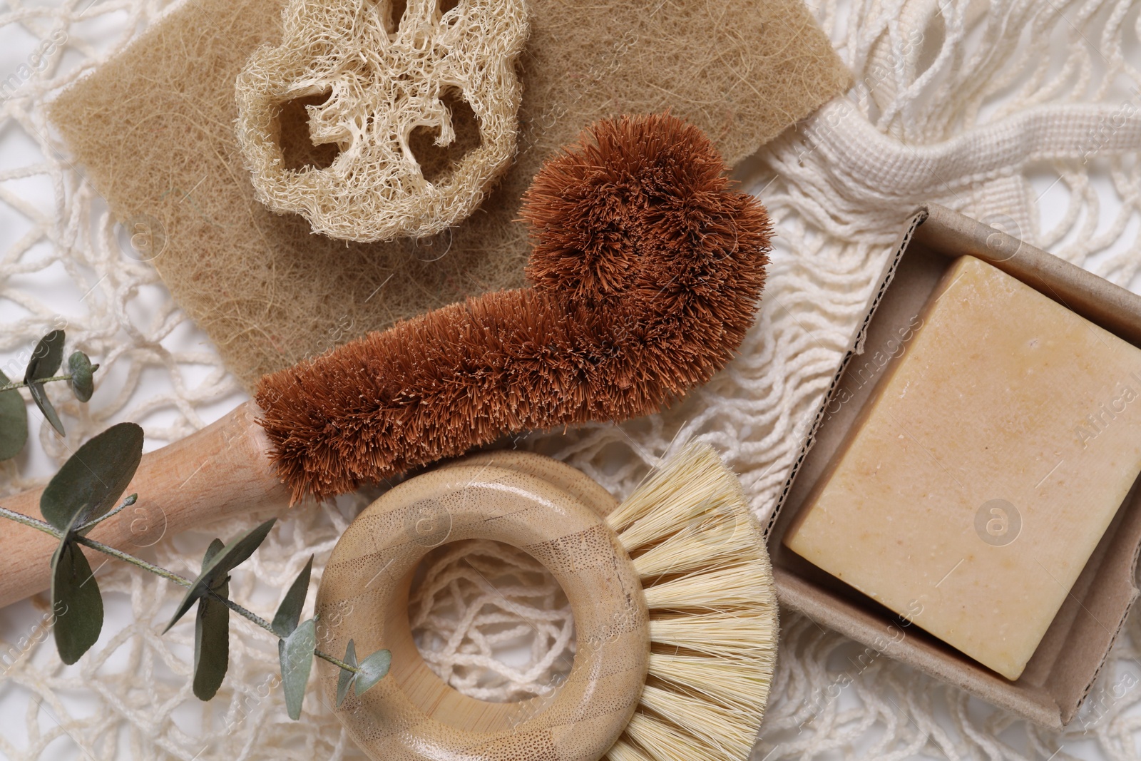 Photo of Cleaning brushes, sponge, loofah, soap bar and eucalyptus leaves on table, top view