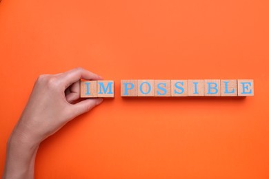 Motivation concept. Woman changing word from Impossible into Possible by removing wooden cubes on orange background, top view