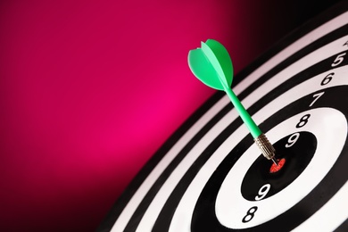 Photo of Green arrow hitting target on dart board against magenta background. Space for text