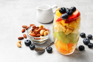 Delicious fruit salad, fresh berries and nuts on light grey table