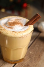 Photo of Tasty eggnog with cinnamon on wooden table against blurred festive lights, closeup