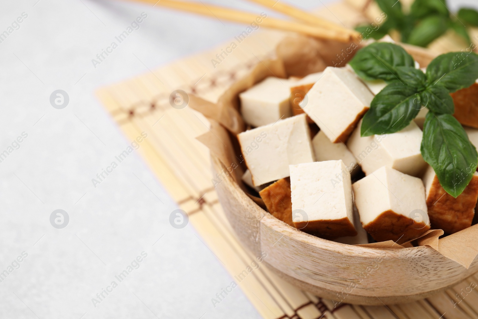 Photo of Bowl of smoked tofu cubes and basil on white table, closeup. Space for text