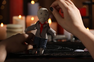Photo of Woman stabbing voodoo doll with pin at table, closeup. Curse ceremony