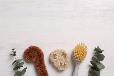 Photo of Cleaning brushes, loofah and eucalyptus leaves on light wooden table, flat lay. Space for text