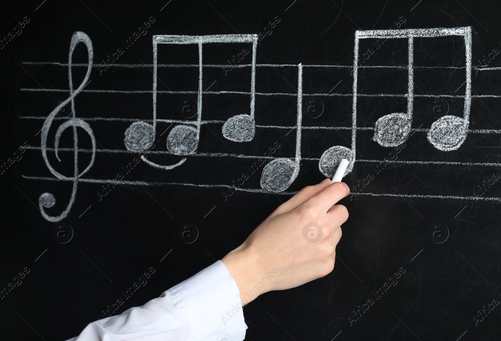 Photo of Woman writing music notes with chalk on blackboard, closeup