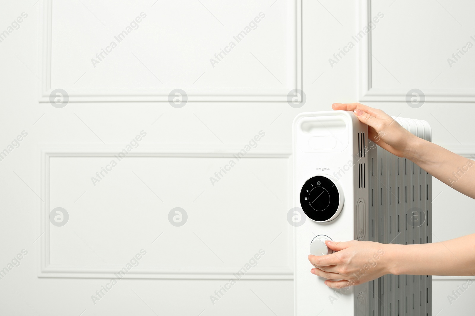 Photo of Young woman adjusting temperature on modern electric heater near white wall, closeup. Space for text