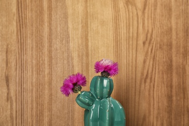Trendy cactus shaped ceramic vase with flowers on wooden background