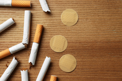 Photo of Nicotine patches and broken cigarettes on wooden table, flat lay