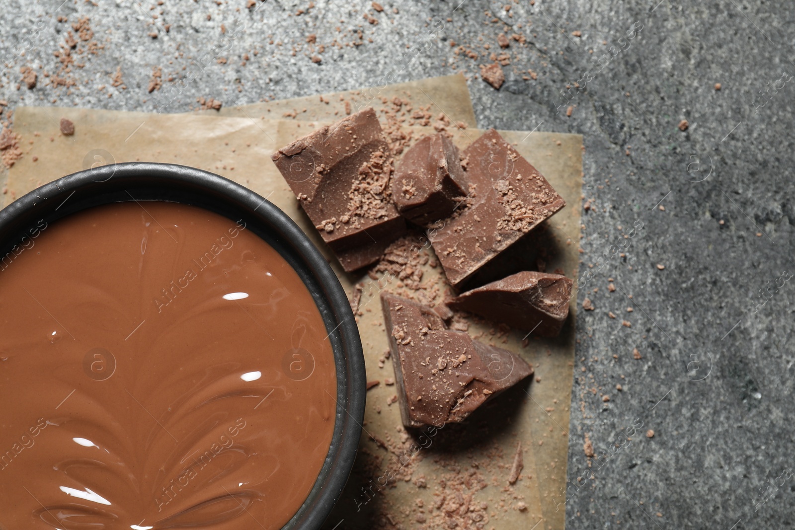 Photo of Tasty milk chocolate paste in bowl and pieces on gray table, top view