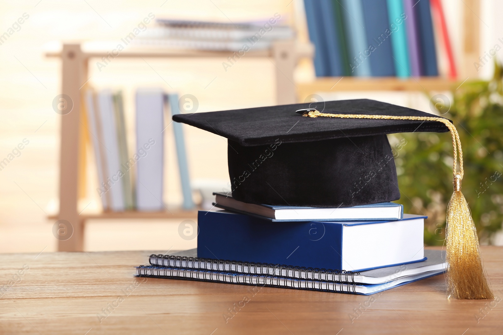 Photo of Graduation hat with books and notebooks on table against blurred background