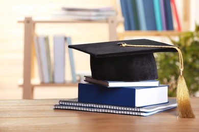 Photo of Graduation hat with books and notebooks on table against blurred background