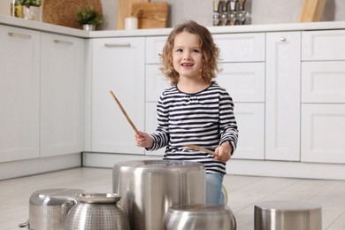 Little girl pretending to play drums on pots in kitchen