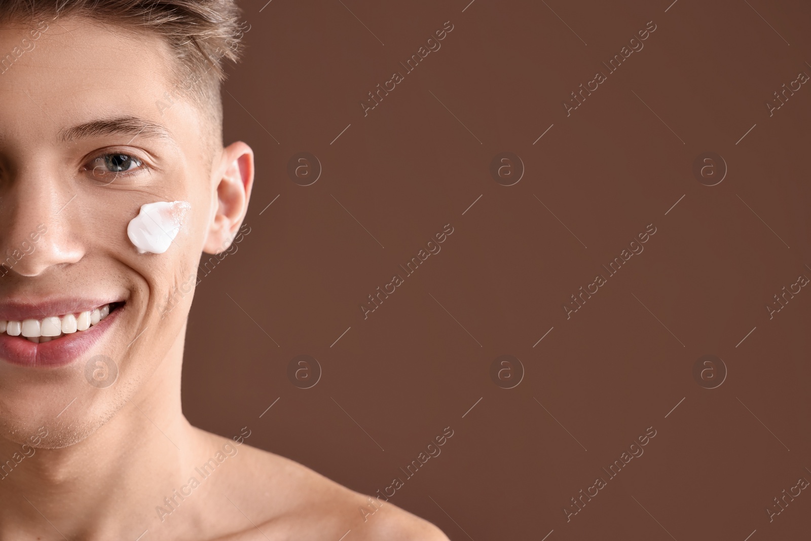 Photo of Handsome man with moisturizing cream on his face against brown background, closeup. Space for text