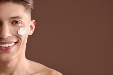 Photo of Handsome man with moisturizing cream on his face against brown background, closeup. Space for text