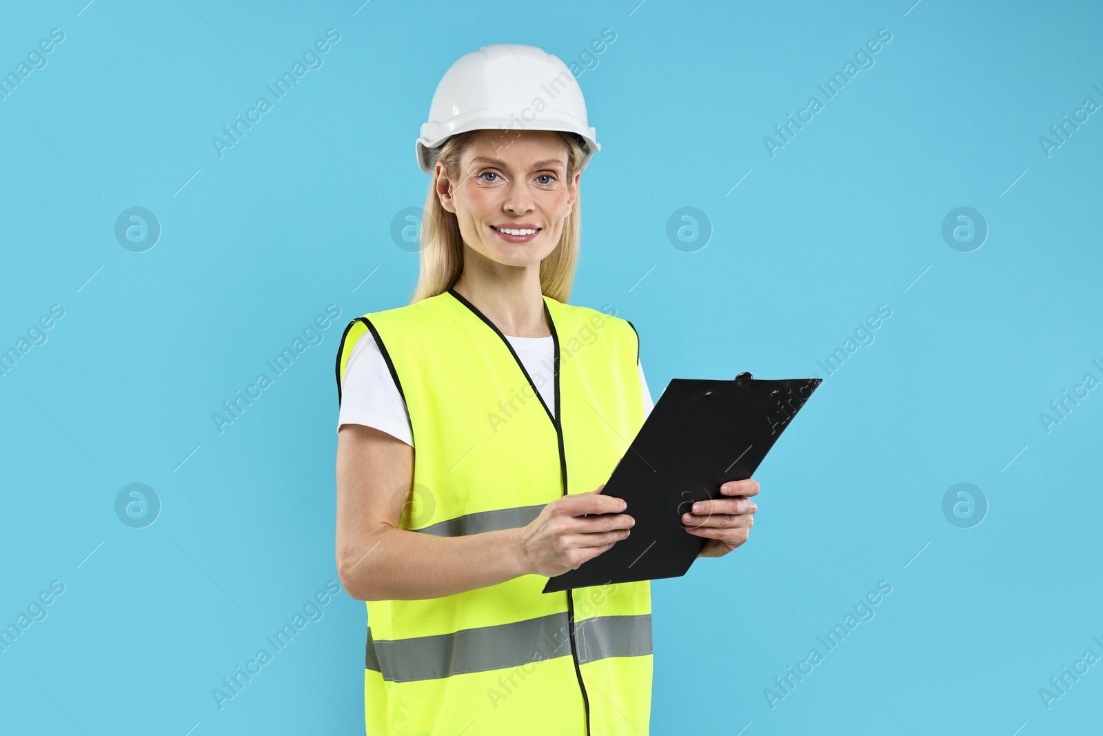 Photo of Engineer in hard hat holding clipboard on light blue background