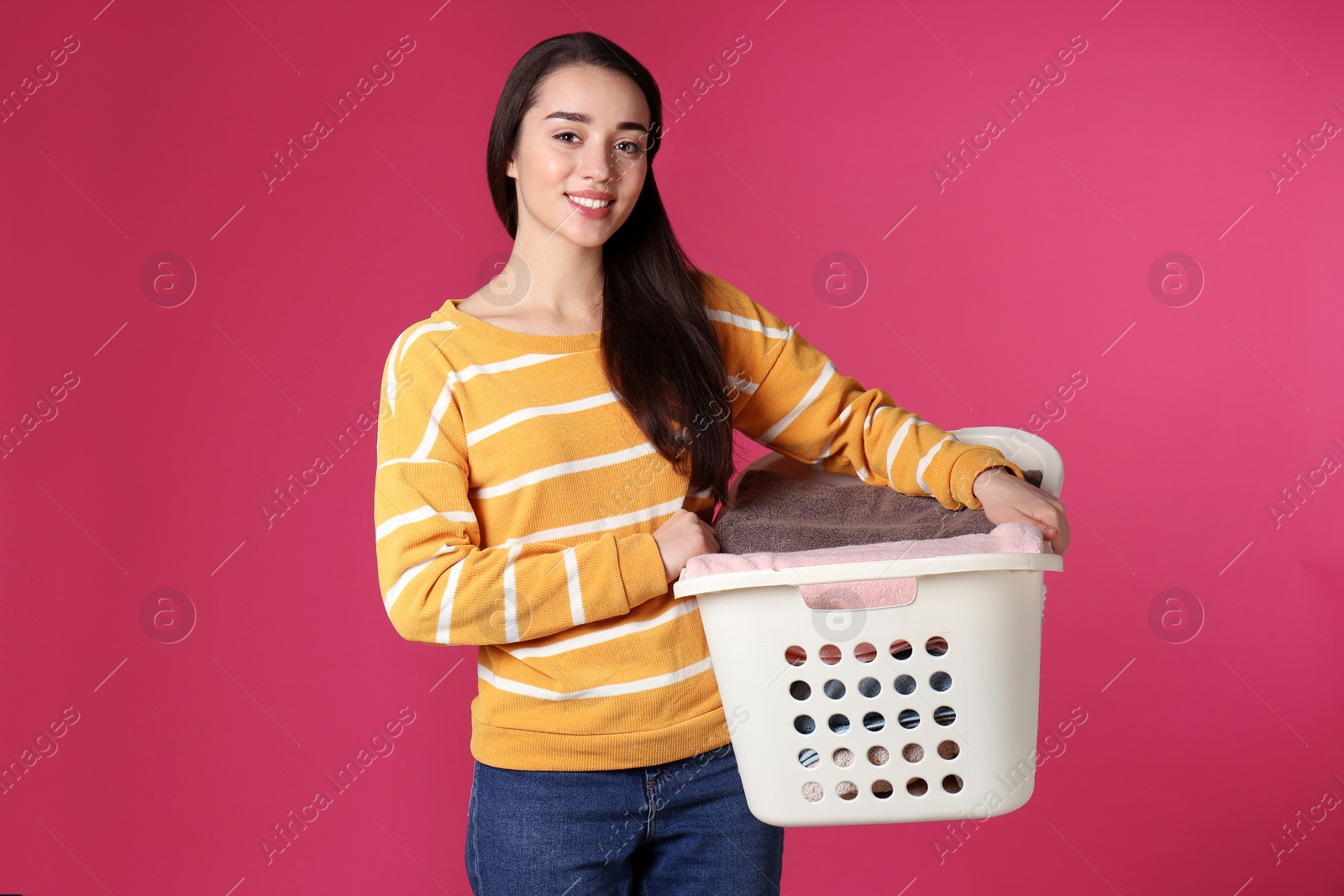 Photo of Happy young woman holding basket with laundry on color background