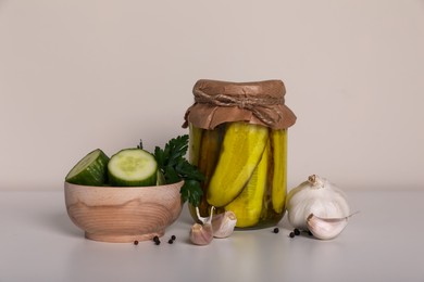 Tasty pickled cucumbers, cut vegetables in wooden bowl and garlic on white table