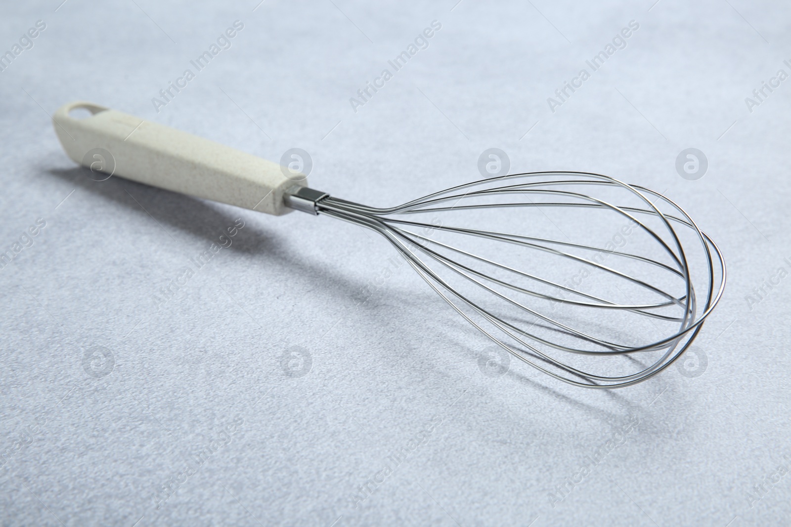 Photo of Metal whisk on gray table. Kitchen tool