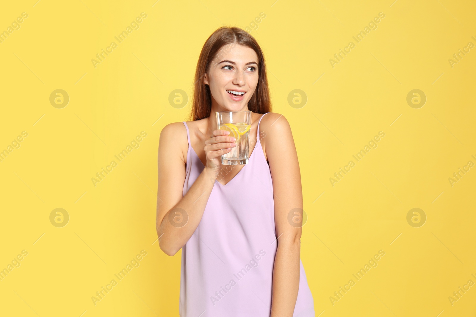 Photo of Young woman with glass of lemon water on yellow background