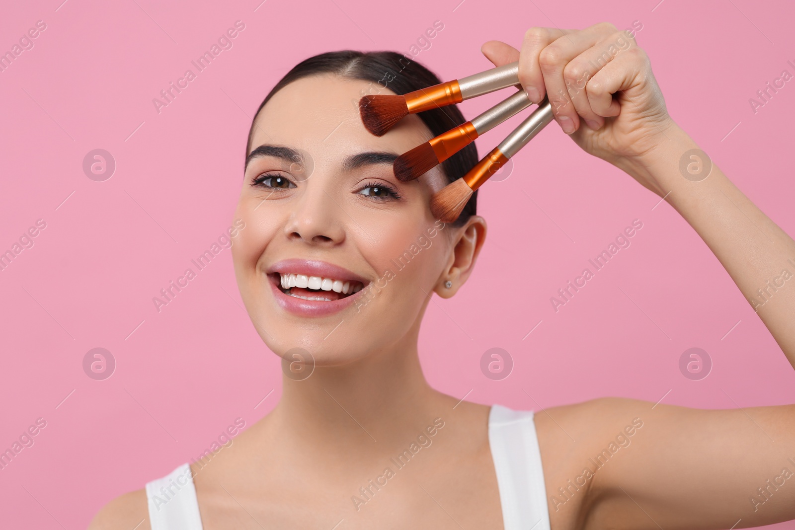 Photo of Happy woman with different makeup brushes on pink background