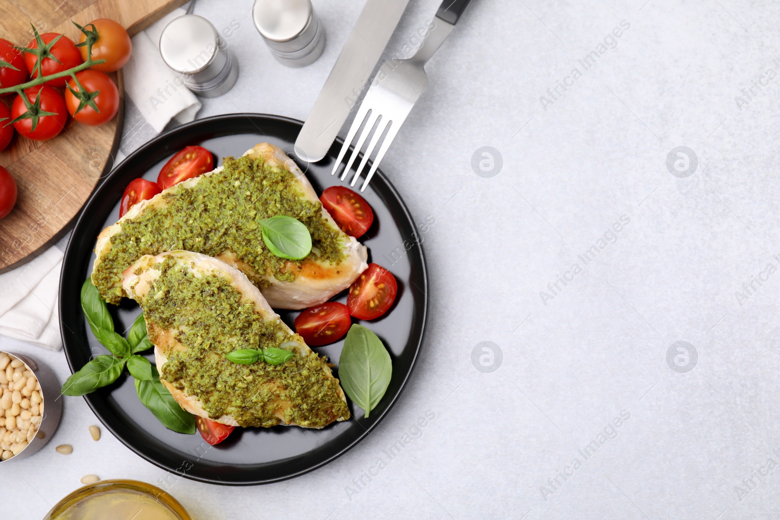 Photo of Delicious chicken breasts with pesto sauce, tomatoes and cutlery served on light gray table, flat lay. Space for text