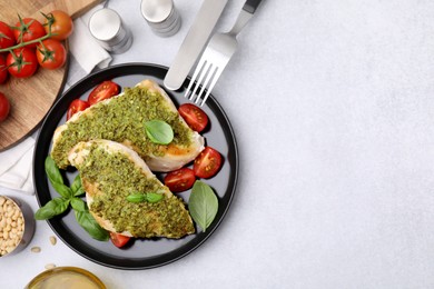 Delicious chicken breasts with pesto sauce, tomatoes and cutlery served on light gray table, flat lay. Space for text