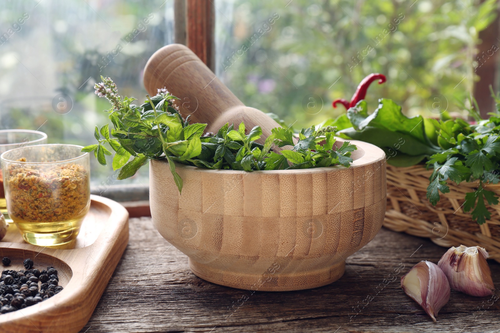 Photo of Mortar with pestle, fresh green herbs and different spices on wooden table near window