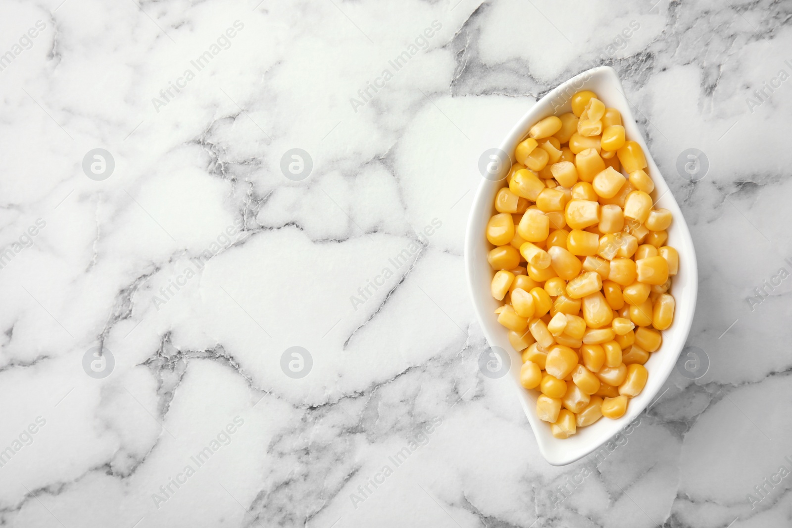 Photo of Bowl with corn kernels on marble background, top view. Space for text