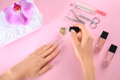 Woman applying nail polish on color background, above view