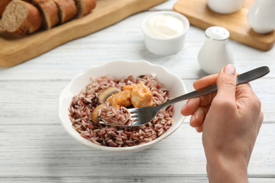 Photo of Woman eating delicious brown rice at white wooden table, closeup