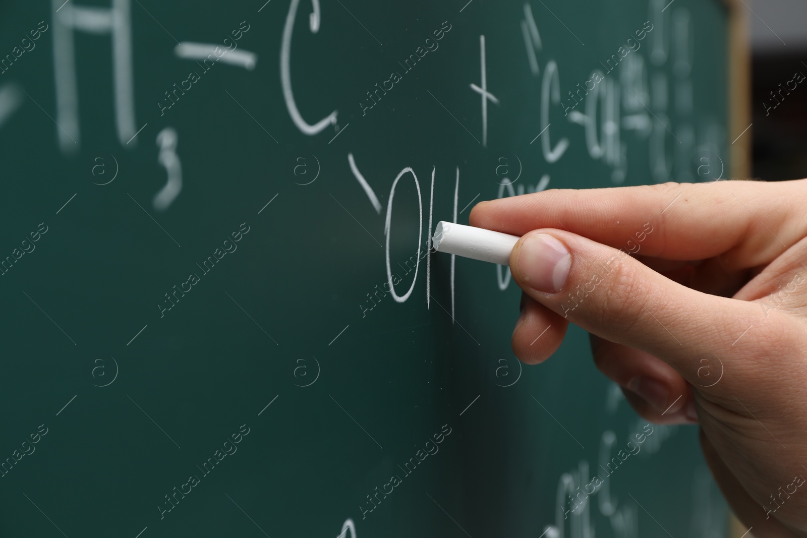 Photo of Teacher writing chemical formulas with chalk on green chalkboard, closeup