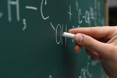 Photo of Teacher writing chemical formulas with chalk on green chalkboard, closeup