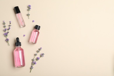 Bottles of essential oil and lavender flowers on beige background, flat lay. Space for text