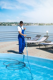Photo of Worker cleaning outdoor swimming pool with underwater vacuum