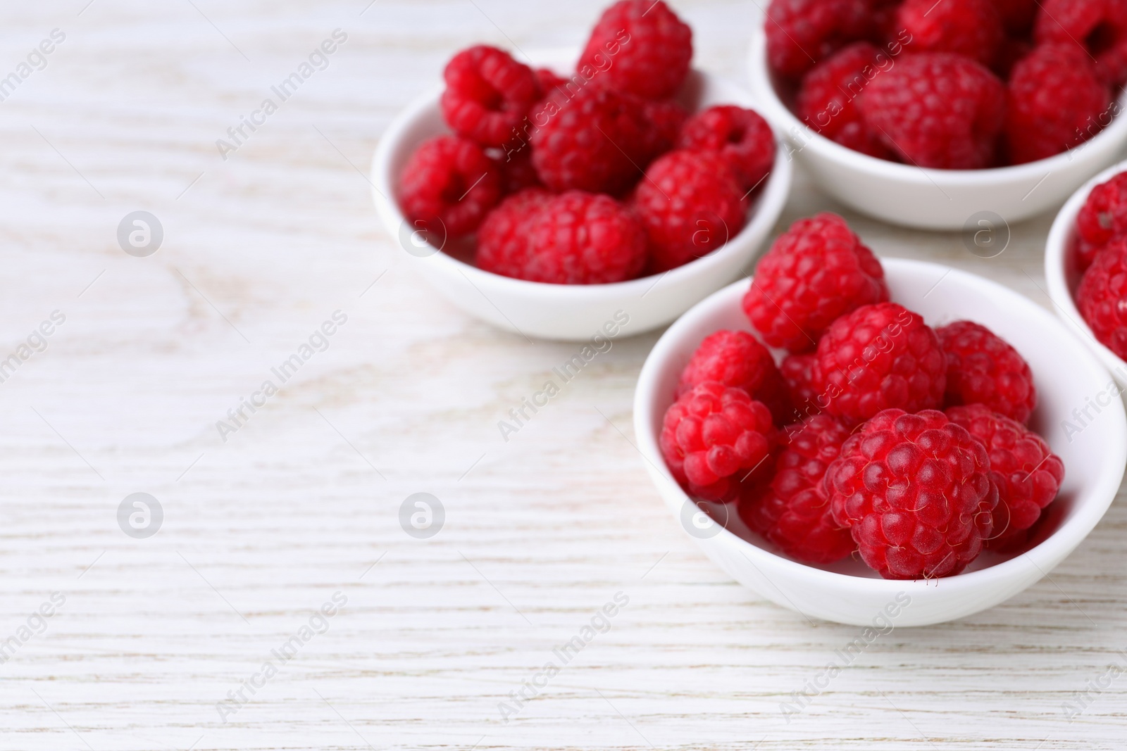 Photo of Tasty ripe raspberries on white wooden table, space for text