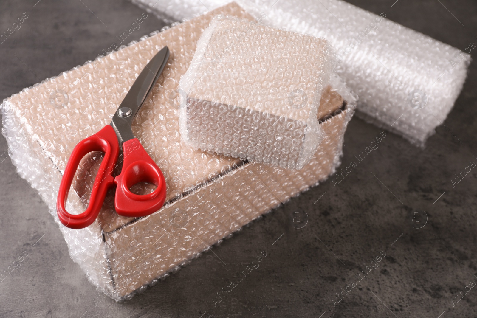 Photo of Cardboard boxes, bubble wrap and scissors on dark grey table