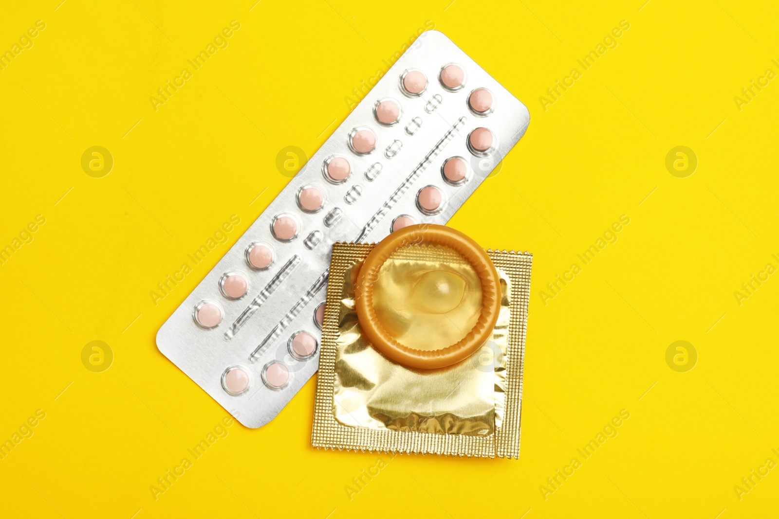 Photo of Condoms and birth control pills on yellow background, flat lay. Safe sex concept