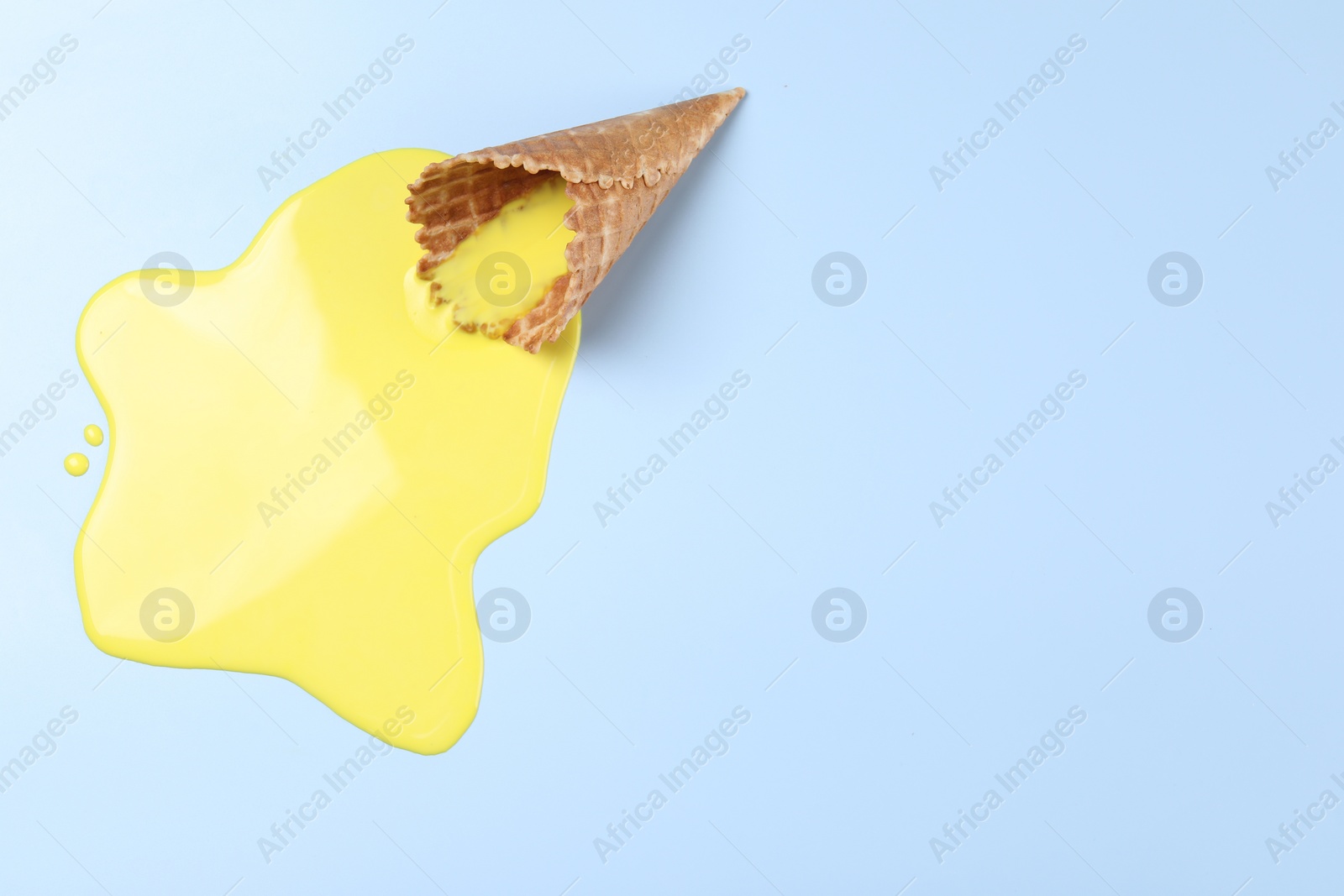 Photo of Melted ice cream and wafer cone on light blue background, top view. Space for text