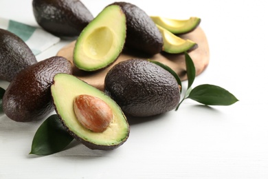 Whole and cut avocados with green leaves on white table