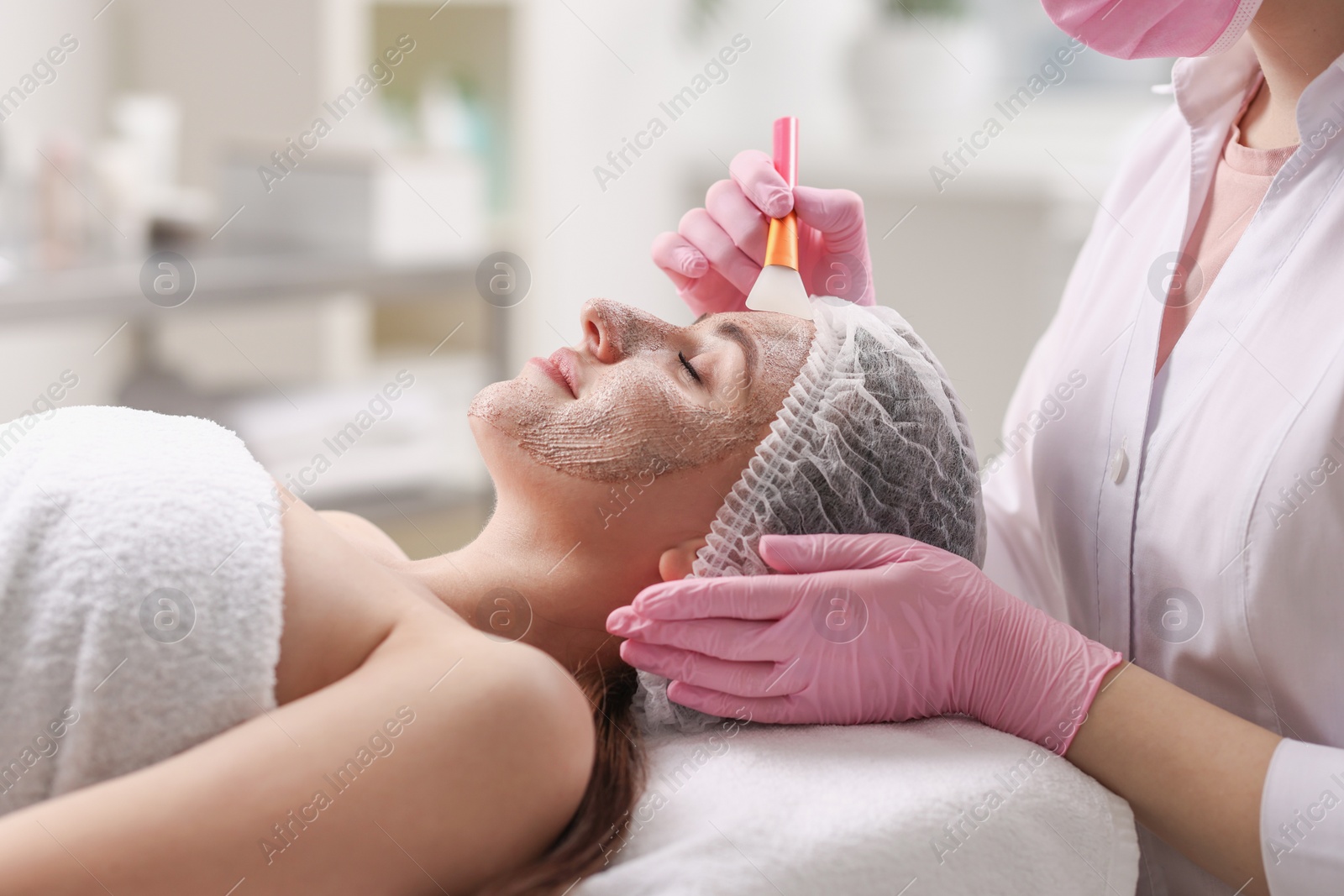 Photo of Cosmetologist applying mask on woman's face in clinic, closeup