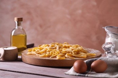 Board with homemade pasta, flour and ingredients on wooden table, space for text