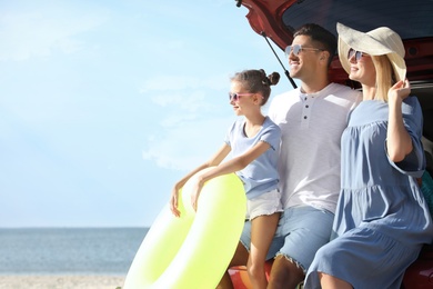 Happy family with inflatable ring near car at beach on sunny day