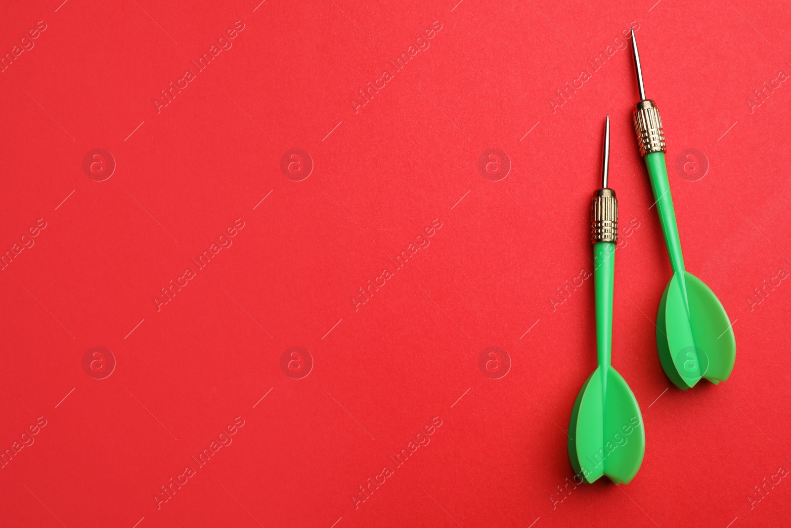 Photo of Green dart arrows on red background, flat lay with space for text