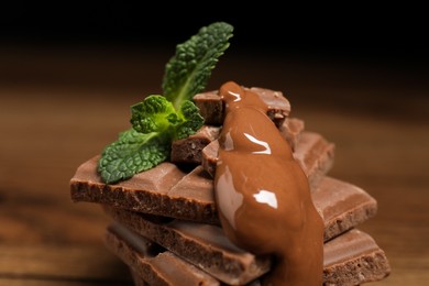 Photo of Pieces of milk chocolate with tasty paste and mint on blurred background, closeup