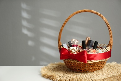 Wicker gift basket with cosmetic products on white table against grey background. Space for text