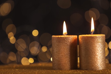 Photo of Burning gold candles on table against blurred lights. Space for text