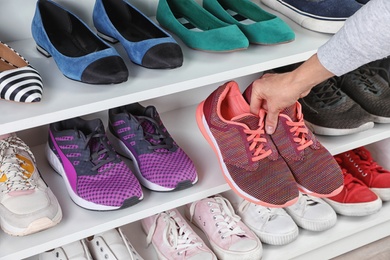 Photo of Woman taking sneakers from shelving unit, closeup