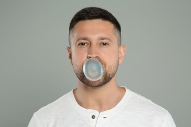 Photo of Handsome man blowing bubble gum on light grey background