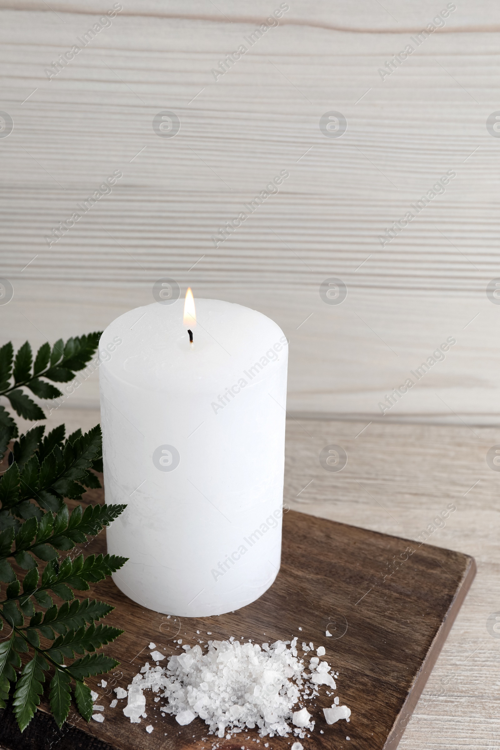 Photo of Burning candle, sea salt and green leaves on light beige wooden table