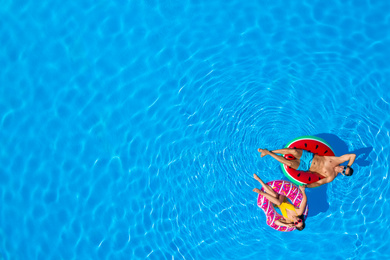 Image of Happy couple with inflatable rings in swimming pool, top view. Space for text 